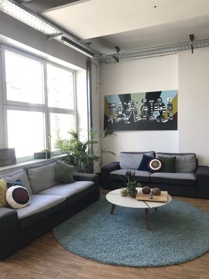 An office corner with bright light coming through large windows, falling on two sofas. There are plants, and art on the walls.